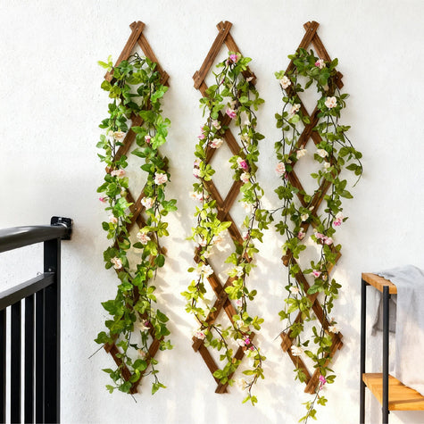 Pink floral garland with green leaves hanging over wall clock, UK home decoration.