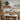A table placed in the center of the kitchen, with a row of cabinets against the wall behind it holding tableware and decorative items. Shelves on the wall also display tableware, and a wreath hangs nearby