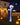 A demon-shaped inflatable stands in the front yard on the grass, with a few jack-o'-lanterns scattered on the ground. The full moon hangs in the dark blue night sky.
