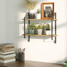 Desk filled with books and a pen holder, industrial-style double wall shelves mounted on the wall holding small potted plants and artwork, creating an artistic vibe