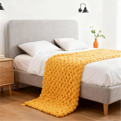Light yellow handwoven chunky knit throw blanket spread on the bed in the bedroom, with a book placed on top, creating a warm and cozy atmosphere